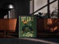 Black-framed Sit Like a Lady print on the floor in front of a dark wooden console
