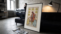 Merchant giving coins to beggars print in a slim black frame leaning on a dark sofa in a concrete print studio