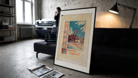 Christmas carollers with star in snowy village print in a slim black frame leaning on a dark sofa in a concrete print studio