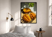 Sliced Mango print in a black frame above a bed with striped linens, a brass wall lamp and a sunlit window