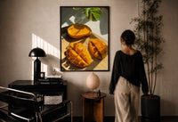 Sliced Mango print in a black frame on a sunlit plaster wall, a woman looking on beside a mushroom lamp