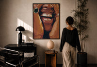 Framed Grillz Smile print in a black frame on a sunlit plaster wall, a woman looking on beside a mushroom lamp