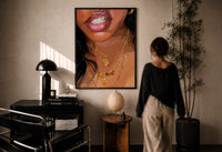 Smile with a Butterfly Pendant print in a black frame on a sunlit plaster wall, a woman looking on beside a mushroom lamp