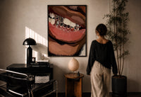 Smile with Silver Grillz print in a black frame on a sunlit plaster wall, a woman looking on beside a mushroom lamp
