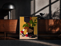 Black-framed Sneakers and a Plant-Filled Tote print on the floor in front of a dark wooden console