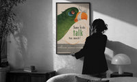 Some Birds Talk Too Much print in a slim black frame being hung on a sunlit wall in a monochrome room