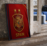 Spain national football crest emblem print in a black frame leaning beside a vintage door on parquet