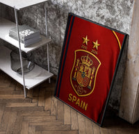 Spain national football crest emblem poster in a black frame leaning beside a shelf in a raw-plaster loft