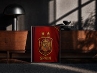 Black-framed Spain national football crest emblem print on a moody console with designer coffee-table books