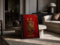 Spain national football crest emblem print in a black frame leaning on a travertine table in a sunlit lounge