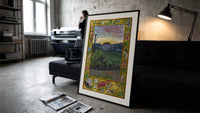 Sunrise over face in landscape print in a slim black frame leaning on a dark sofa in a concrete print studio