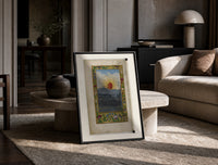 Sun with human face over town print in a black frame leaning on a travertine table in a sunlit lounge