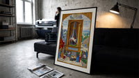 Alchemical flask with birds inside print in a slim black frame leaning on a dark sofa in a concrete print studio