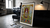 Three-headed dragon in alchemical flask print in a slim black frame leaning on a dark sofa in a concrete print studio