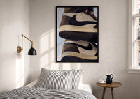 Stacked Brown and Cream Sneakers print in a black frame above a bed with striped linens