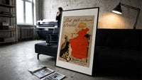 Girl in red dress drinking from bowl print in a slim black frame leaning on a dark sofa in a concrete print studio