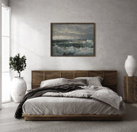 Crashing ocean waves on rocks print in a dark wood frame above a rattan bed on a plaster wall
