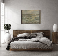 Rough seascape with breaking waves print in a dark wood frame above a rattan bed on a plaster wall