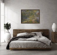 Sunlit garden path by cottage print in a dark wood frame above a rattan bed on a plaster wall