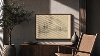 Sailing ships in a harbor print in a wood frame above a fluted sideboard beside an olive tree