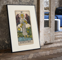 Winged angel pouring water between cups print in a black frame leaning beside a vintage door on parquet