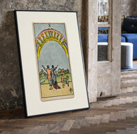 Ten of Cups tarot family print in a black frame leaning beside a vintage door on parquet