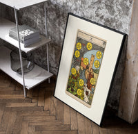 Ten of Pentacles tarot card poster in a black frame leaning beside a shelf in a raw-plaster loft