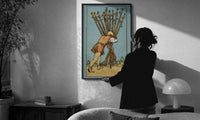 Ten of Wands print in a slim black frame being hung on a sunlit wall in a monochrome room