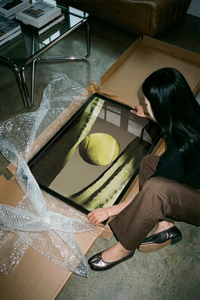 Woman unboxing the tennis and cactus minimal sports poster from a flat cardboard shipping box