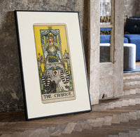 The Chariot tarot card figure print in a black frame leaning beside a vintage door on parquet