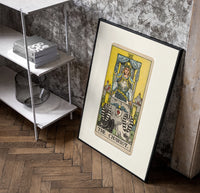 The Chariot tarot card figure poster in a black frame leaning beside a shelf in a raw-plaster loft