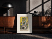 Black-framed The Chariot tarot card figure print on a moody console with designer coffee-table books