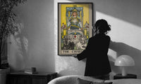 The Chariot print in a slim black frame being hung on a sunlit wall in a monochrome room