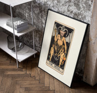 The Devil tarot card figure poster in a black frame leaning beside a shelf in a raw-plaster loft