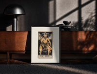 Black-framed The Devil tarot card figure print on a moody console with designer coffee-table books
