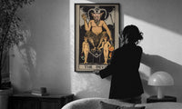 The Devil print in a slim black frame being hung on a sunlit wall in a monochrome room
