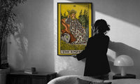 The Empress print in a slim black frame being hung on a sunlit wall in a monochrome room