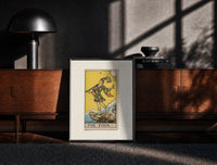 Black-framed The Fool tarot card figure print on a moody console with designer coffee-table books