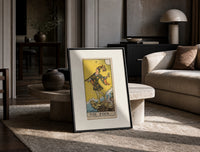 The Fool tarot card figure print in a black frame leaning on a travertine table in a sunlit lounge