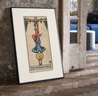 Man hanging upside down from tree print in a black frame leaning beside a vintage door on parquet