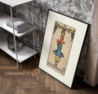 Man hanging upside down from tree poster in a black frame leaning beside a shelf in a raw-plaster loft