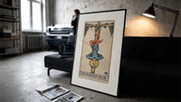 Man hanging upside down from tree print in a slim black frame leaning on a dark sofa in a concrete print studio