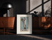 Black-framed Cloaked hermit holding lantern and staff print on a moody console with designer coffee-table books