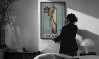 The Hermit print in a slim black frame being hung on a sunlit wall in a monochrome room