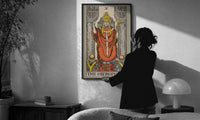 The Hierophant print in a slim black frame being hung on a sunlit wall in a monochrome room