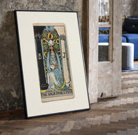 The High Priestess tarot figure print in a black frame leaning beside a vintage door on parquet