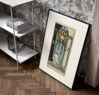 The High Priestess tarot figure poster in a black frame leaning beside a shelf in a raw-plaster loft
