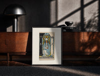 Black-framed The High Priestess tarot figure print on a moody console with designer coffee-table books