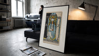 The High Priestess tarot figure print in a slim black frame leaning on a dark sofa in a concrete print studio