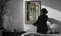 The High Priestess print in a slim black frame being hung on a sunlit wall in a monochrome room